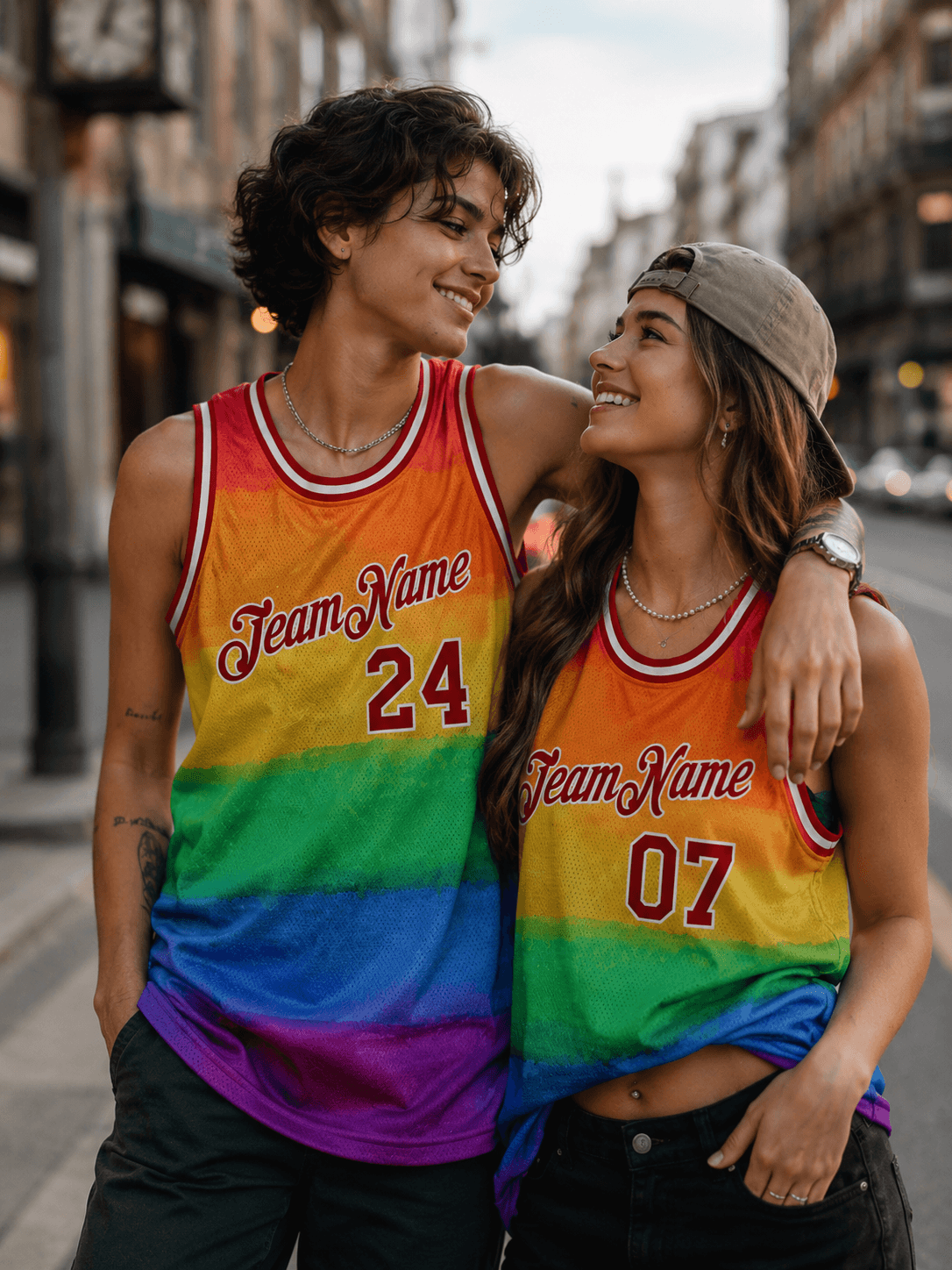 A happy couple standing together on a city street, wearing vibrant rainbow pride basketball jerseys with numbers.