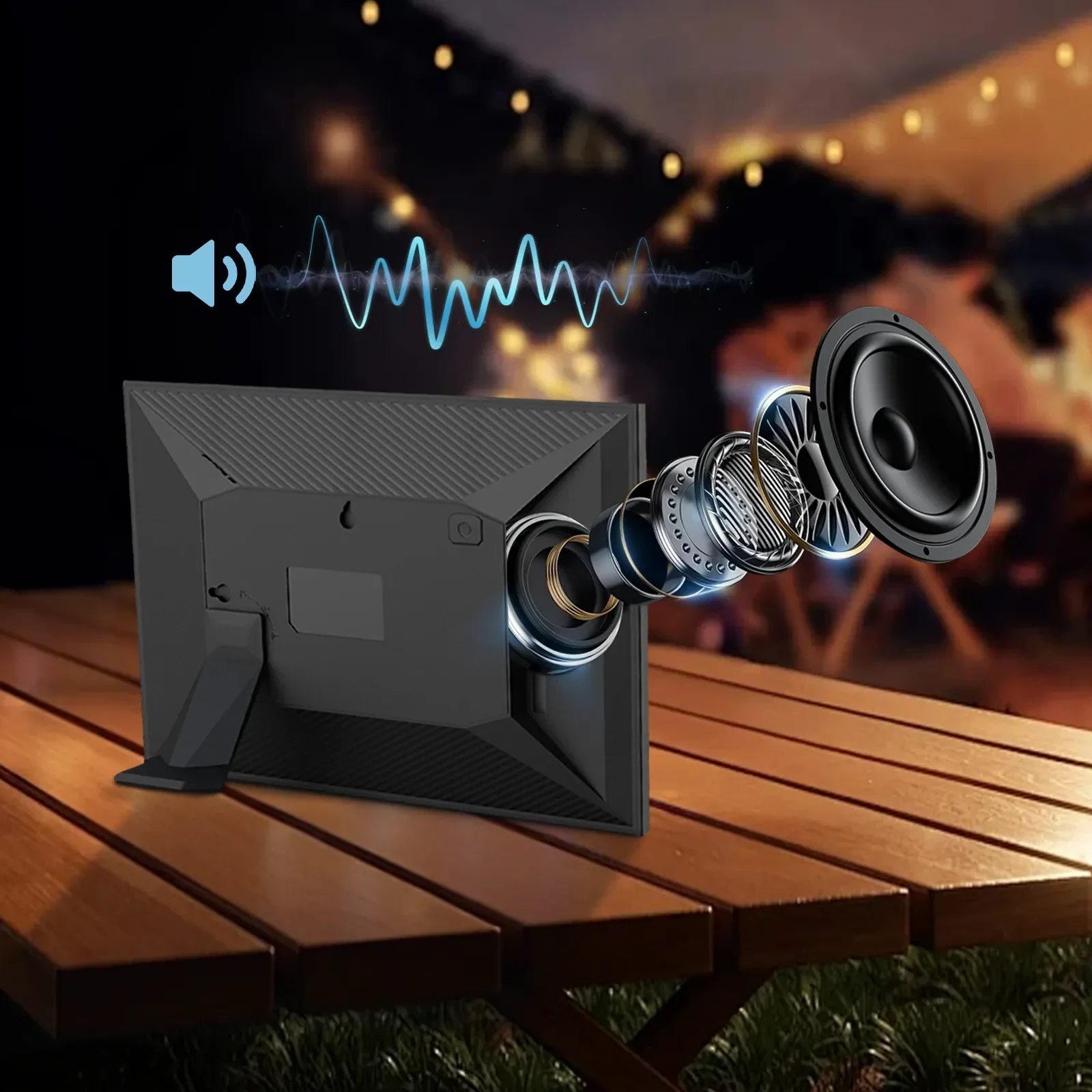 Black portable speaker with exploded internal components on wooden outdoor table at night with string lights.