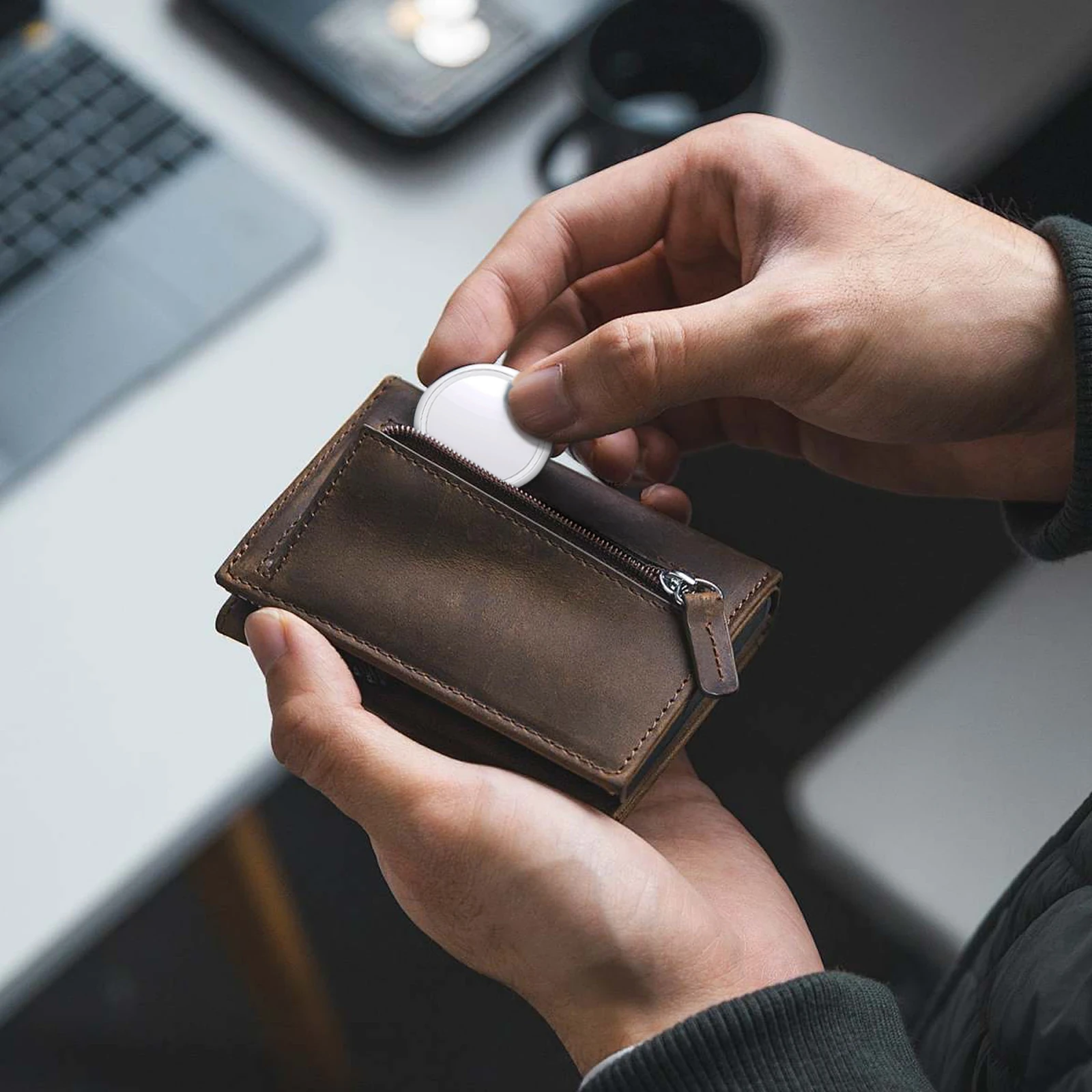 Person placing a white tracker into a brown leather zip wallet.