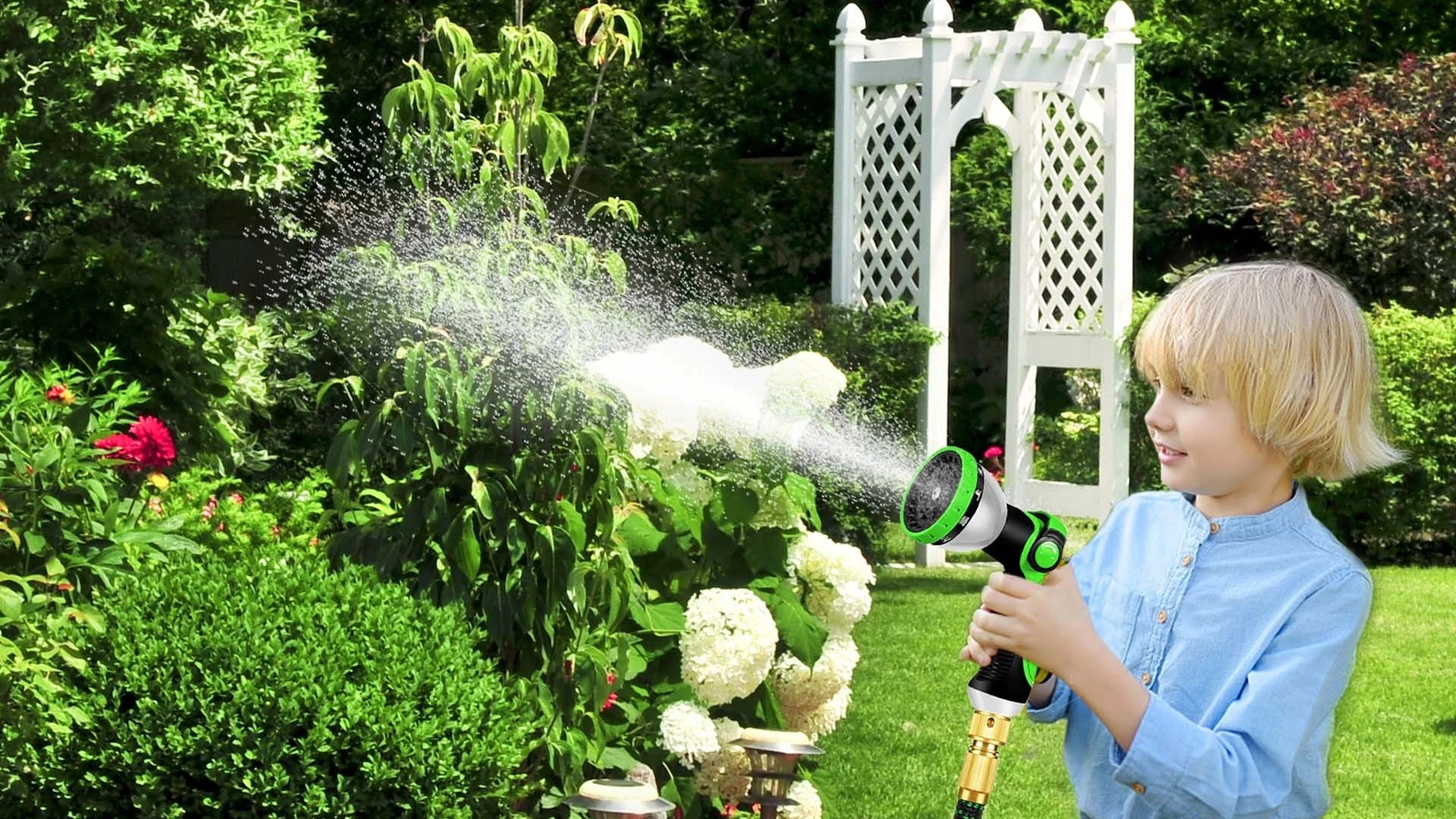 Child using green and black garden hose spray nozzle to water plants in sunny backyard garden with white arbor.