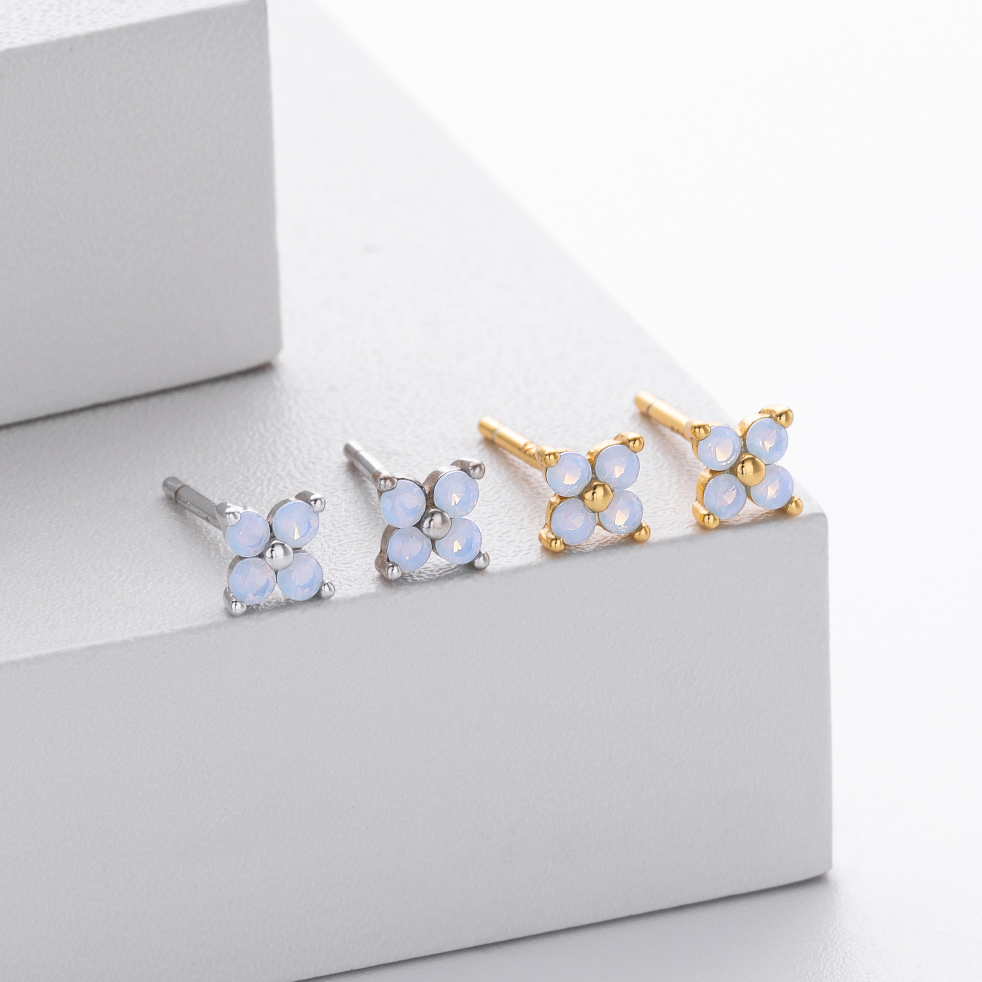 ese delicate stud earrings feature a charming four-petal flower design with faceted light blue