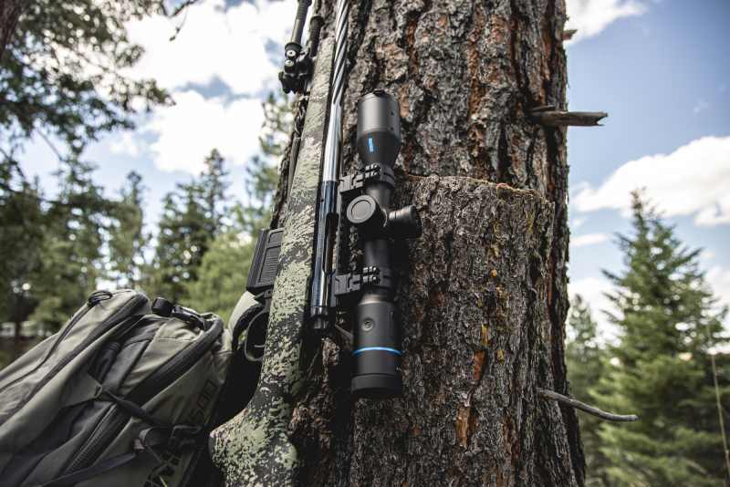 Side angle of Night Stalker EX Weapon Mounted Scope leaning against a tree.