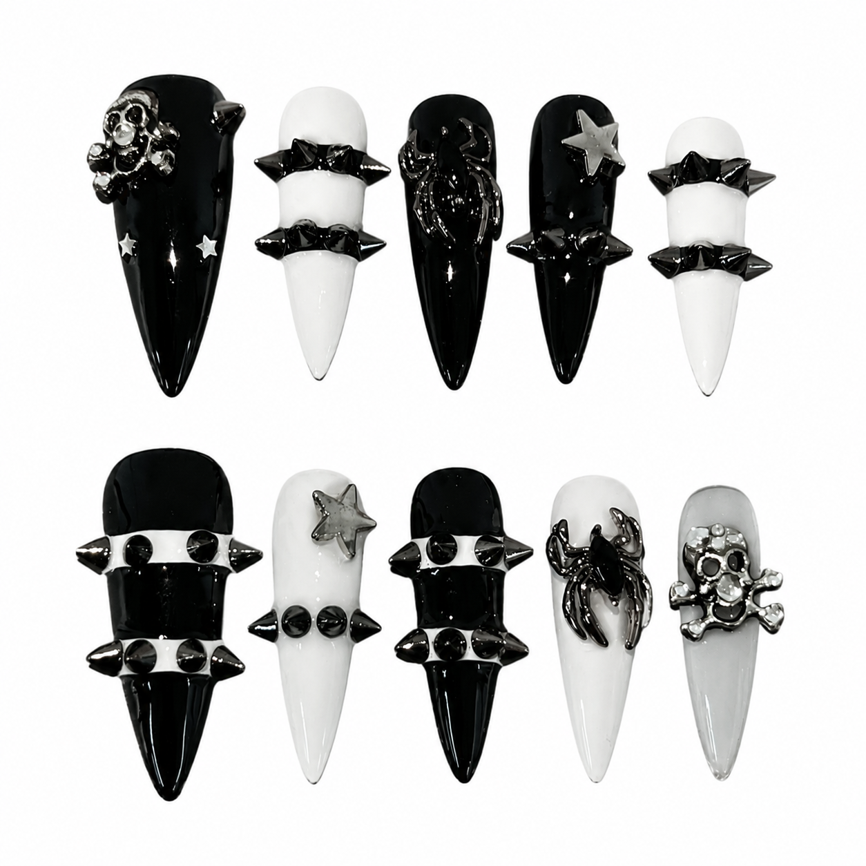 Glossy black and white stiletto press-on nails featuring heavy metal cone spikes, gunmetal spider charms, rhinestoned skulls, and star studs.