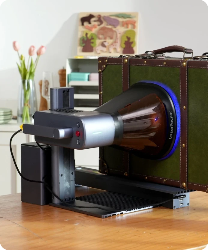 LaserPecker LP2 Plus laser engraver with a 90-degree adjustable stand, rotating horizontally to engrave a custom design on a large vintage green suitcase.