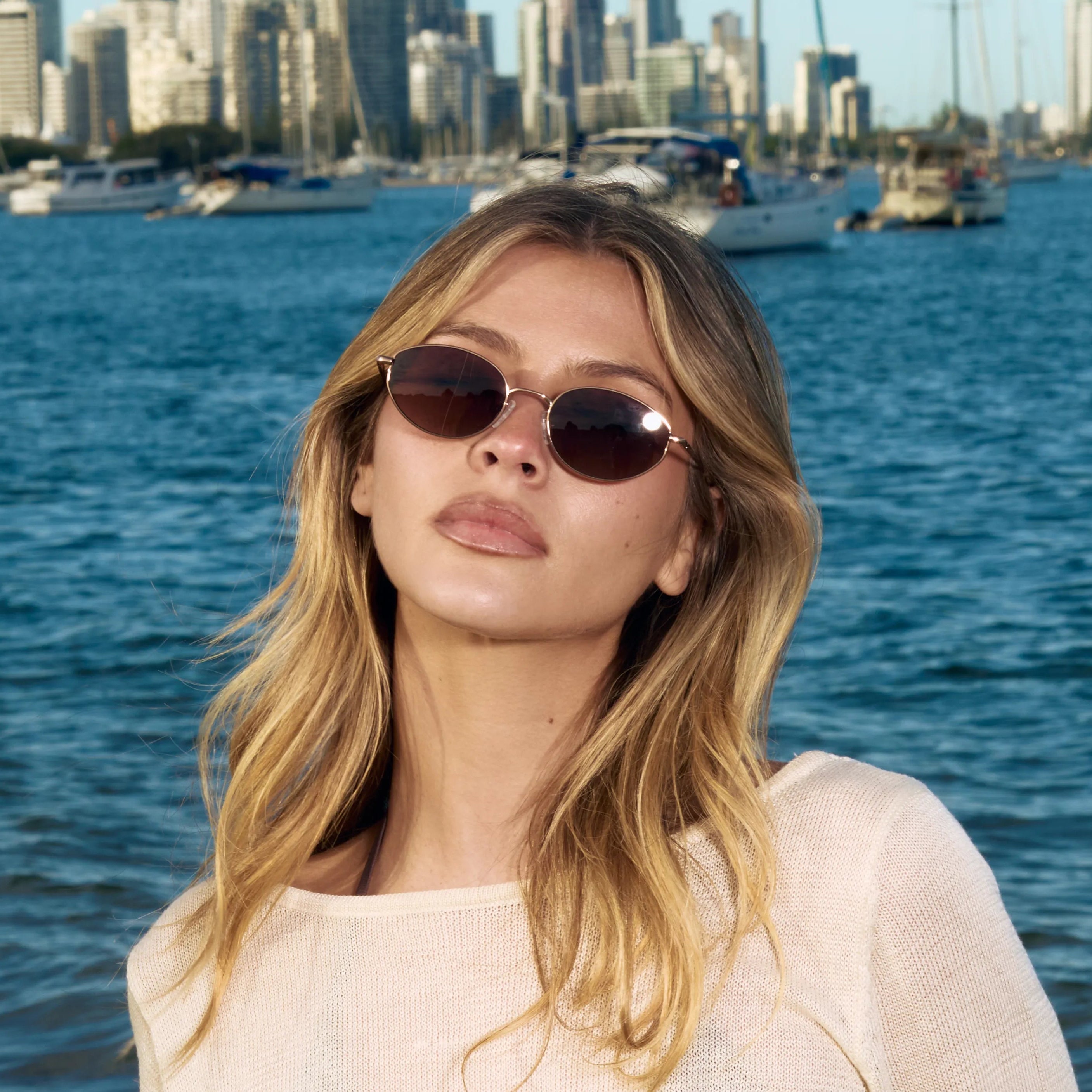 Woman wearing sunglasses with a city skyline and water in the background