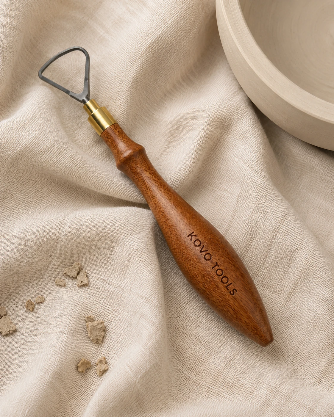 Triangle shape carbide trimming tool on linen background with clay trimming shavings
