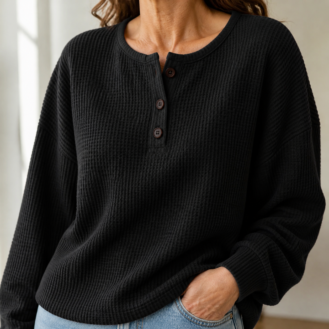 Close-up of the Black waffle-knit texture three-button neckline cuff and curved hem