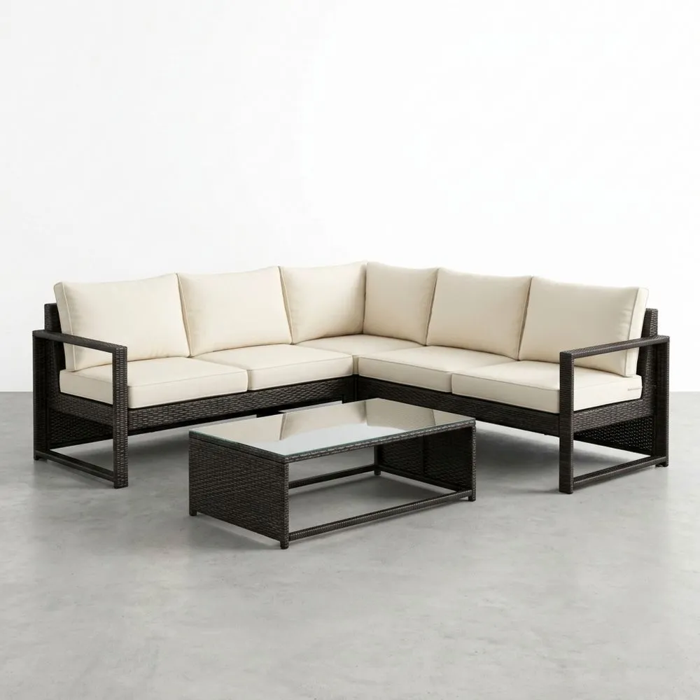 Sofá esquinero de ratán sintético con cojines crema y mesa de vidrio templado