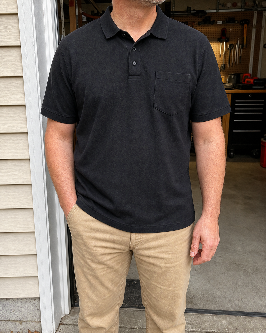 Broad build model wearing the Workwear Black classic-fit piqué pocket polo shirt at an open garage workshop doorway