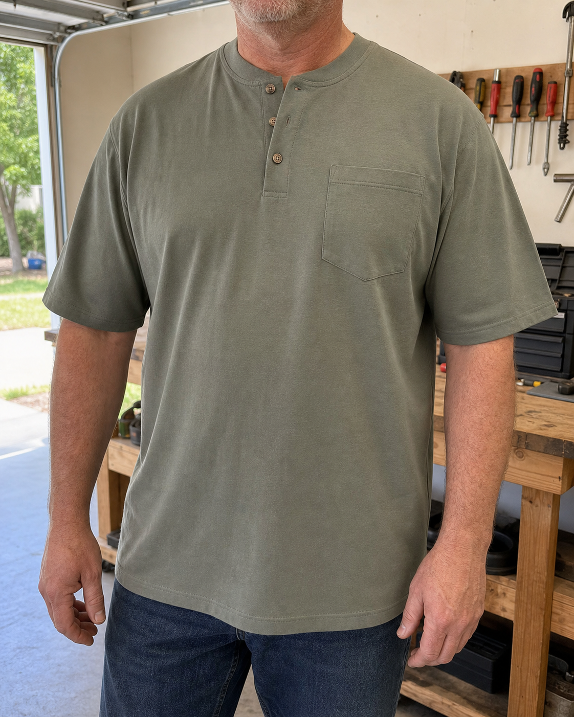 Stocky model wearing the moss olive three-button pocket Henley in a bright home garage
