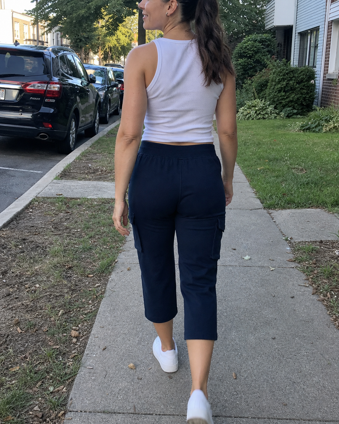 Tessa, a tall woman, wearing Midnight Navy stretch cargo capri pants while walking on a neighborhood sidewalk