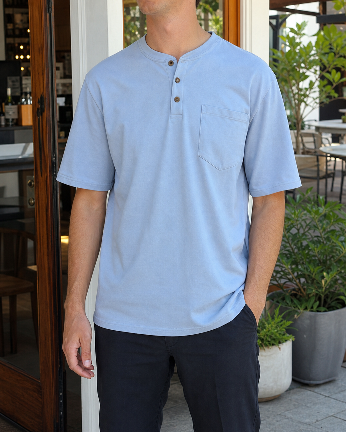 Slim model wearing the steel blue three-button pocket Henley at a bright cafe patio