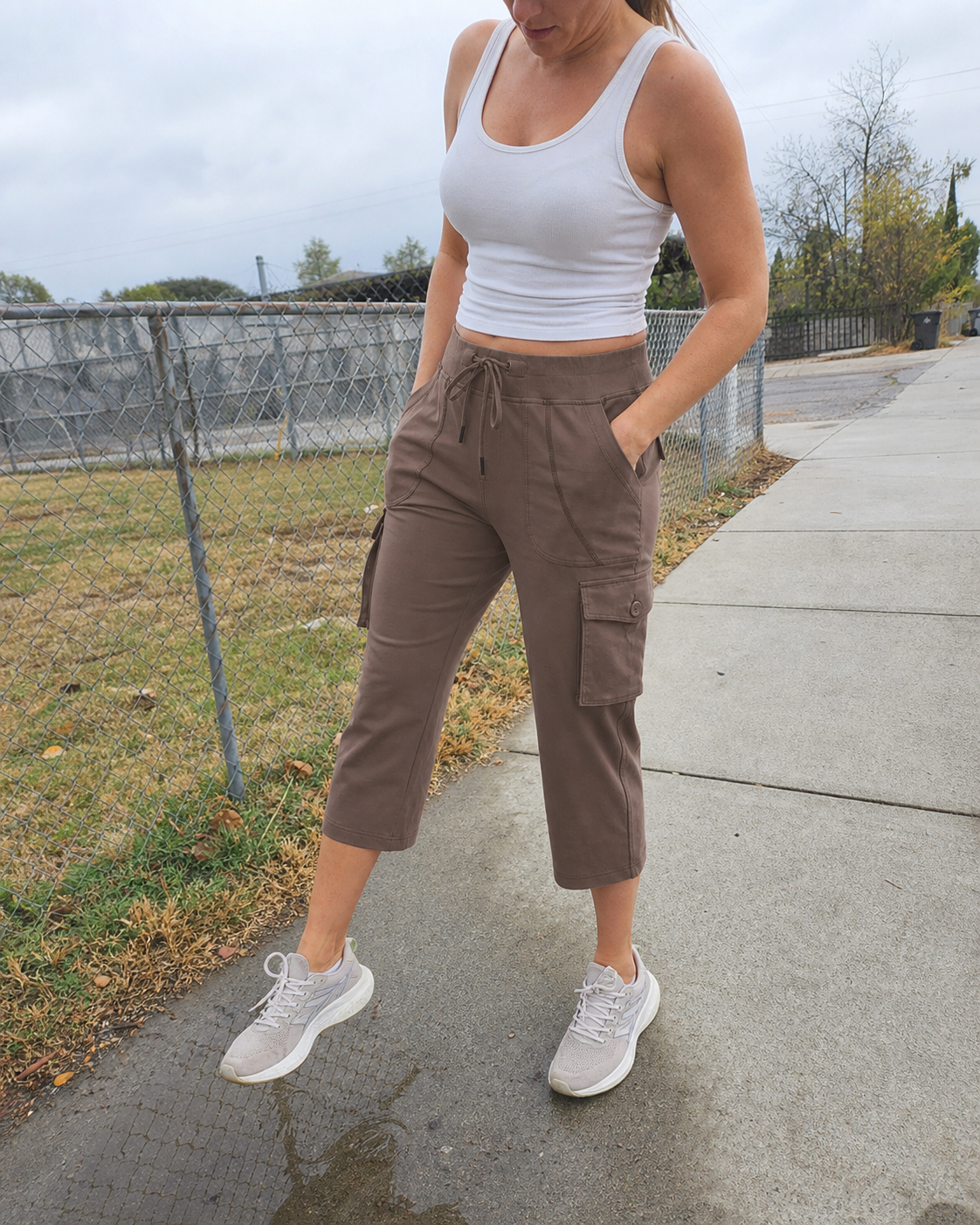 Zoe, an athletic woman, wearing Mocha Brown stretch cargo capri pants beside a neighborhood sidewalk puddle