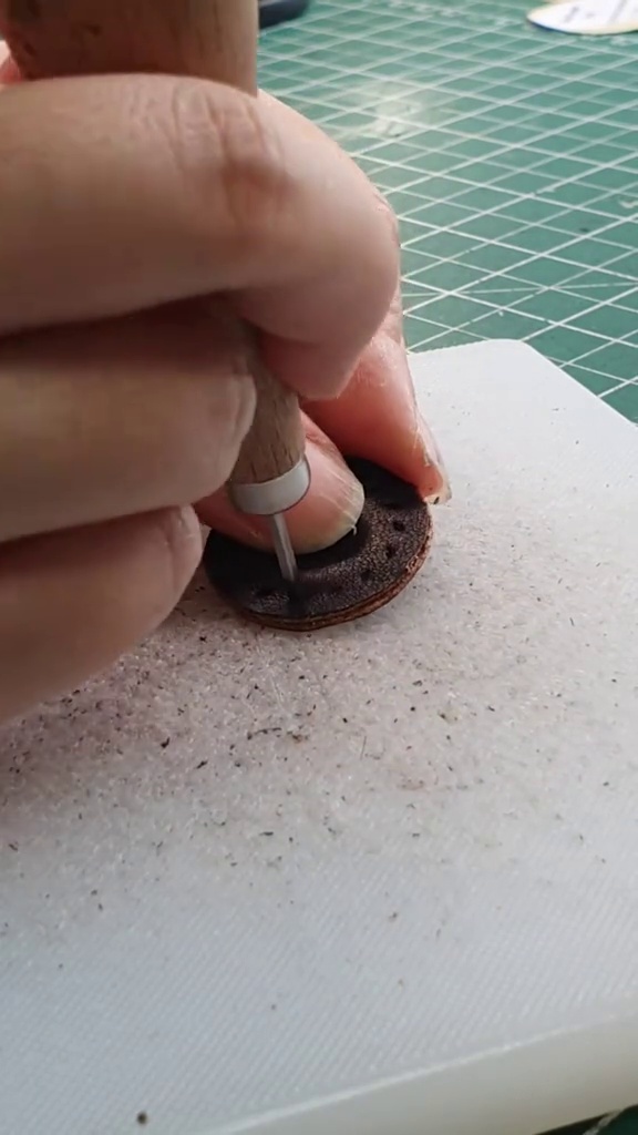 Macro view of small leather detail piece being punched for clean stitch holes