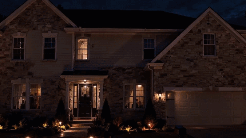 Image suggestion: wide nighttime photo of a two-story home covered with vivid Halloween ghost, pumpkin, witch, bat, and haunted-house projections
