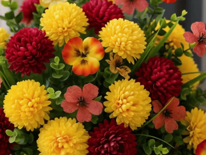 Wide hero image of a welcoming front porch decorated with a full artificial fall flower arrangement in yellow, red, orange, and coral