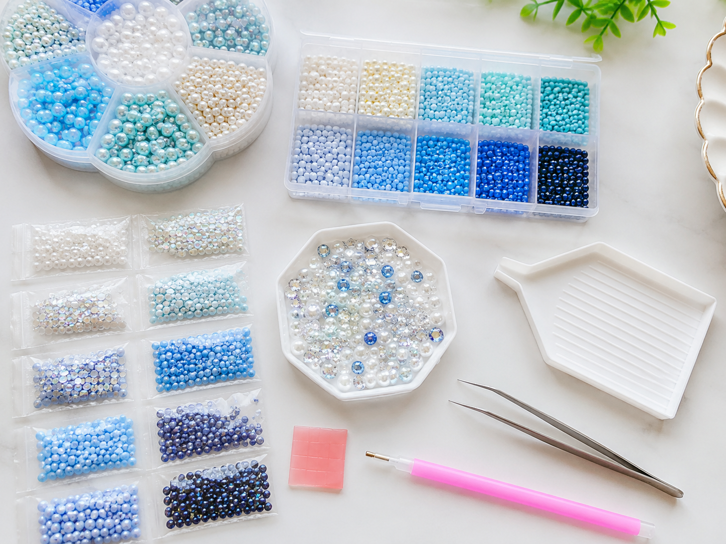 Overhead photo of sorted pearls, decorative beads, rhinestones, wax pad, and placement pen ready to use