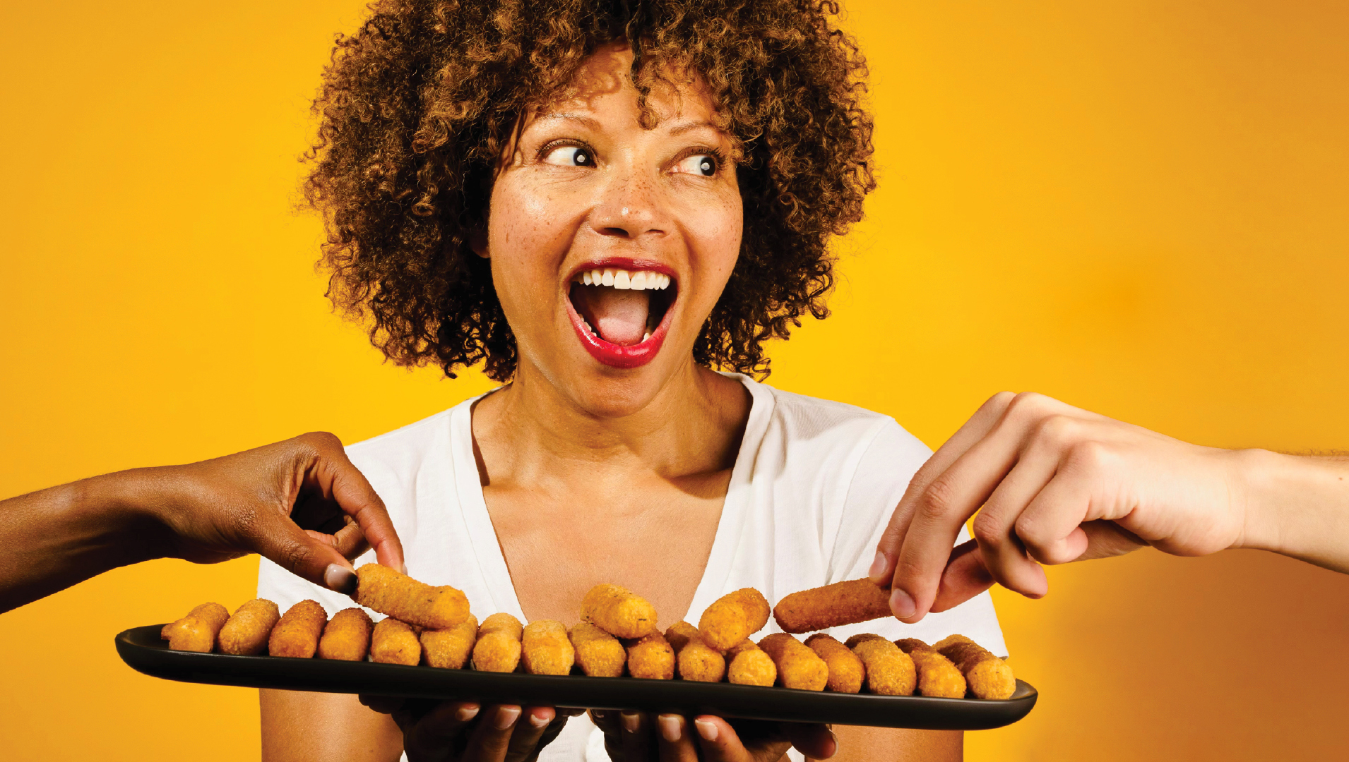 A delighted woman holding a tray of fried mozzarella sticks as hands reach in