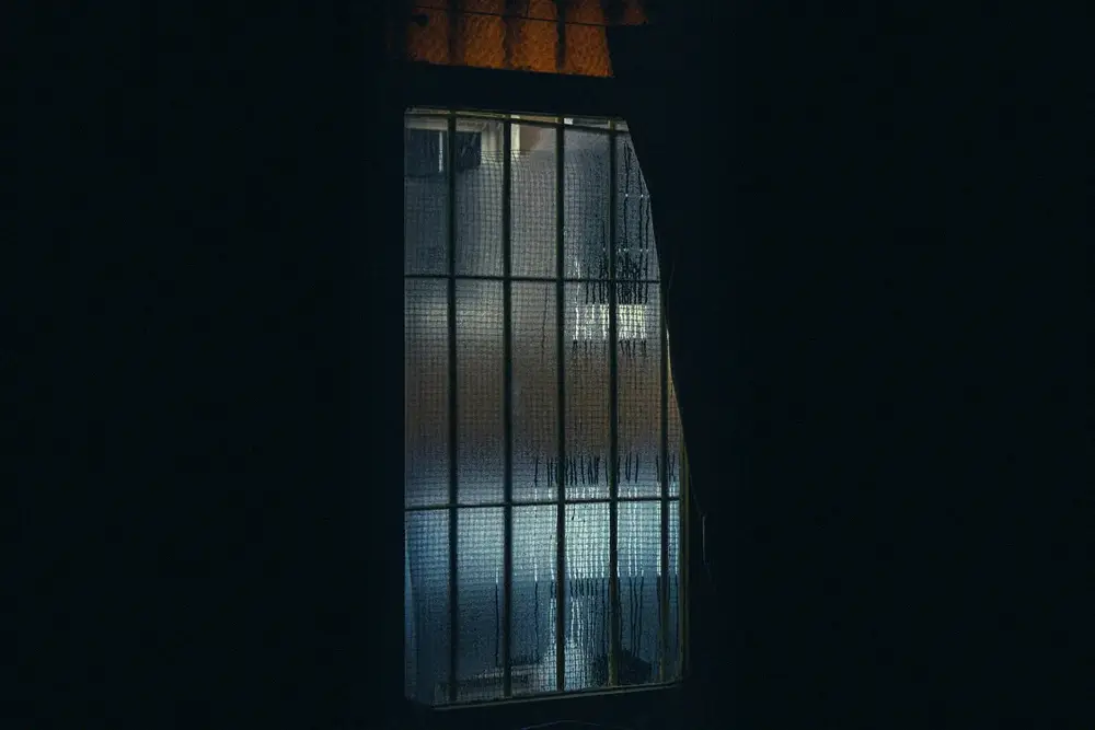 Water droplets and condensation covering a textured indoor window.