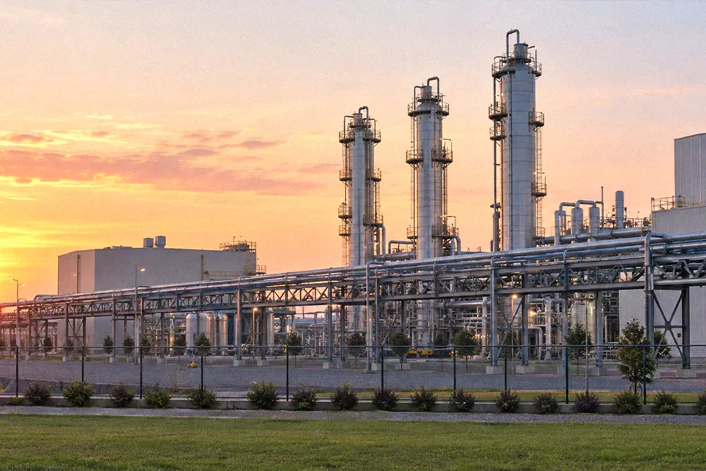 Silver processing towers and elevated pipe racks at an industrial facility at sunrise.