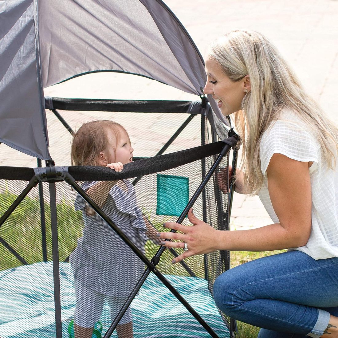 Parent beside a child in the playpen under its removable canopy