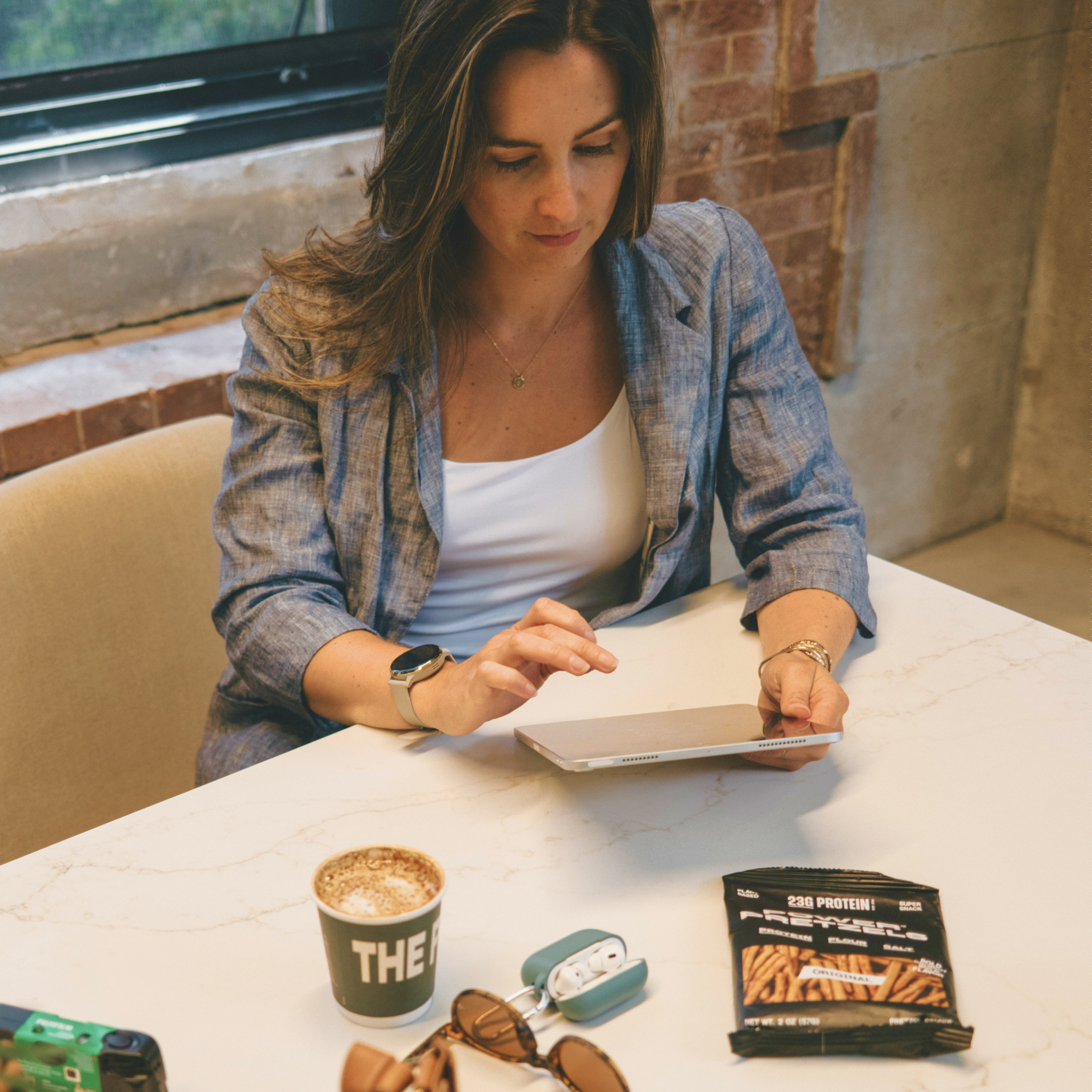 Woman at a café table with a tablet, coffee and an Original bag