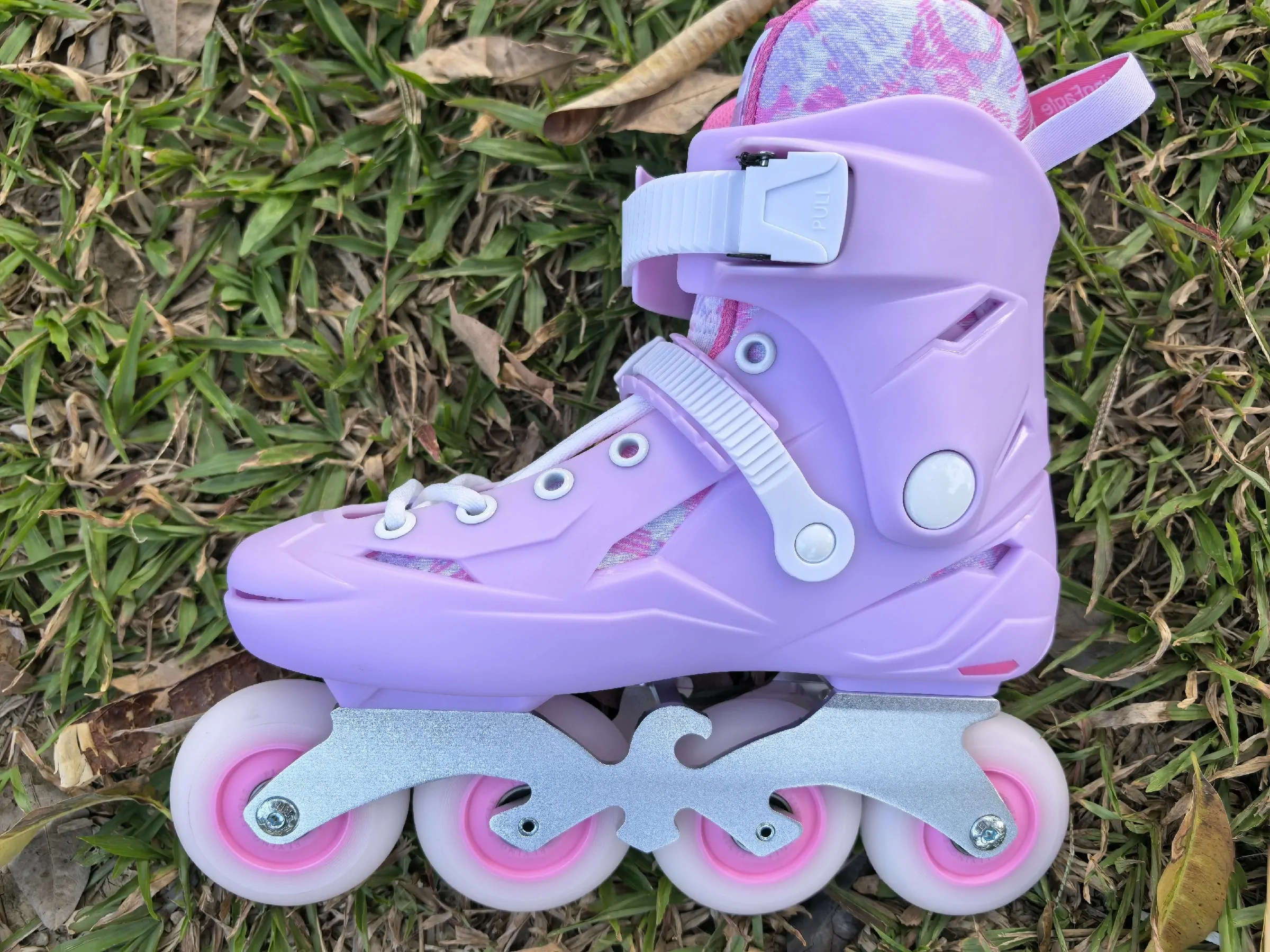 Purple Flying Eagle inline skate with white buckles, silver frame and four white wheels with pink hubs, photographed on grass