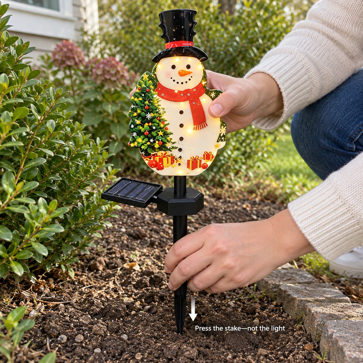 Hands pressing the black ground stake into loose soil