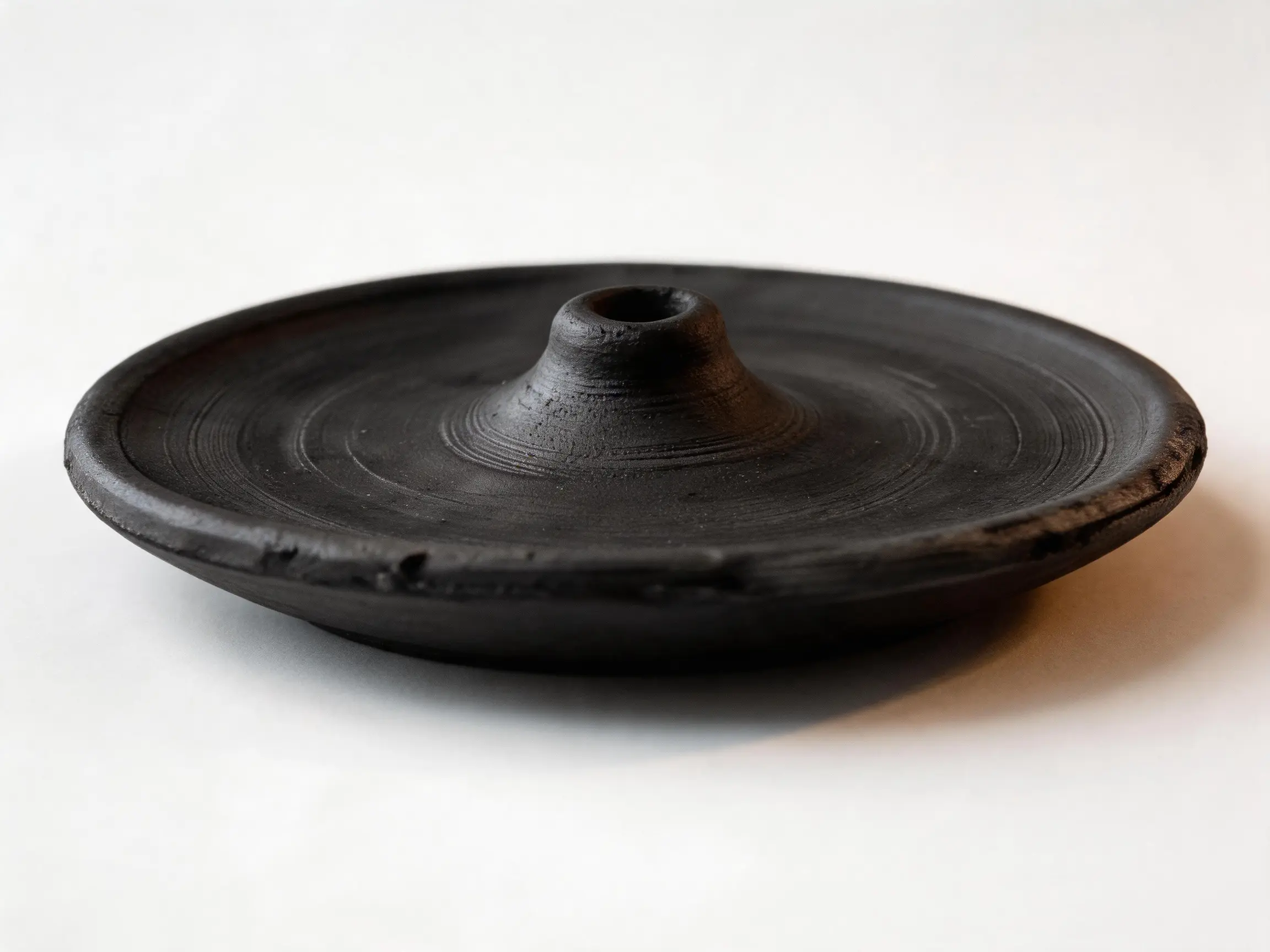 Low angled view of the Dawa black pottery incense tray, showing its shallow rim and central opening