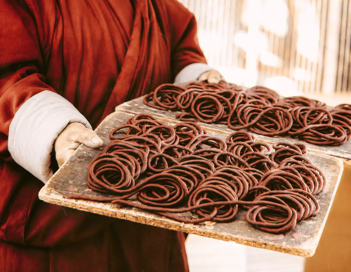 Close-up of hands holding a worn wooden tray covered with burgundy coils of incense material.