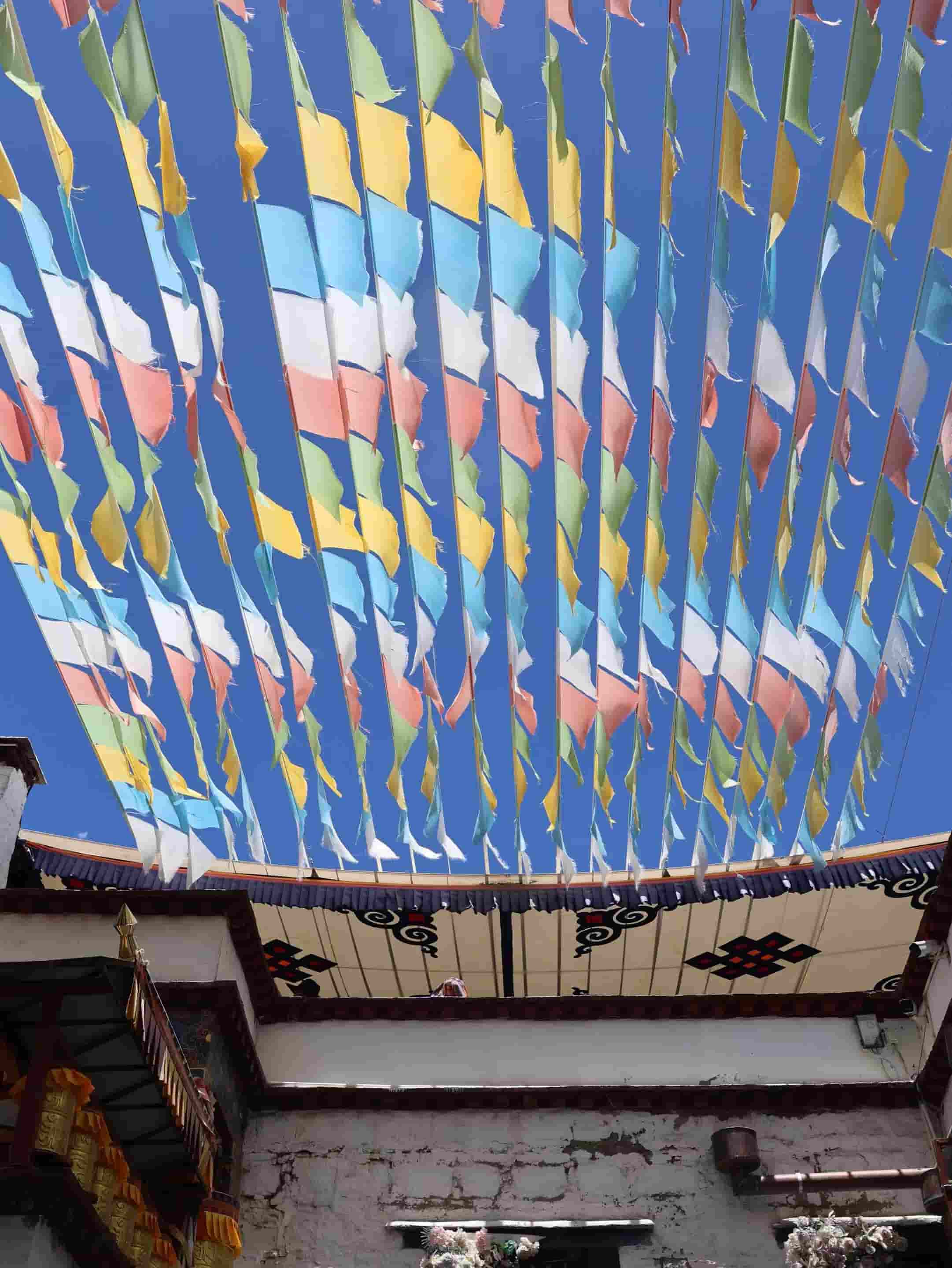 Colorful prayer flags strung above a courtyard beneath a clear blue sky.