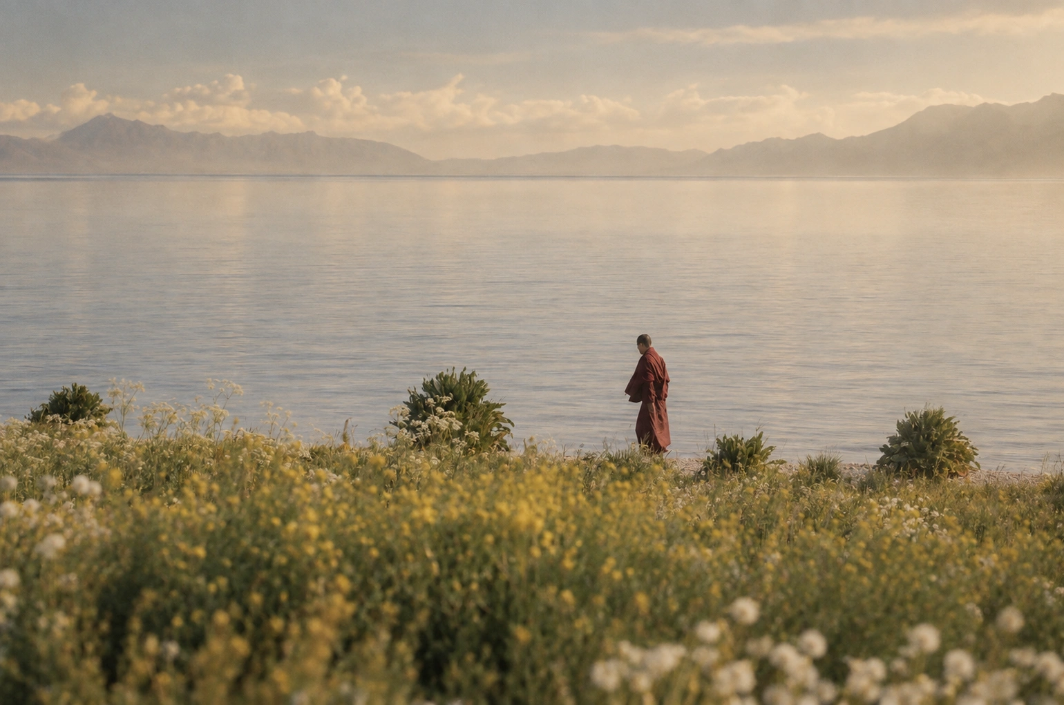 A monk walking beside a lake in a mountain landscape.