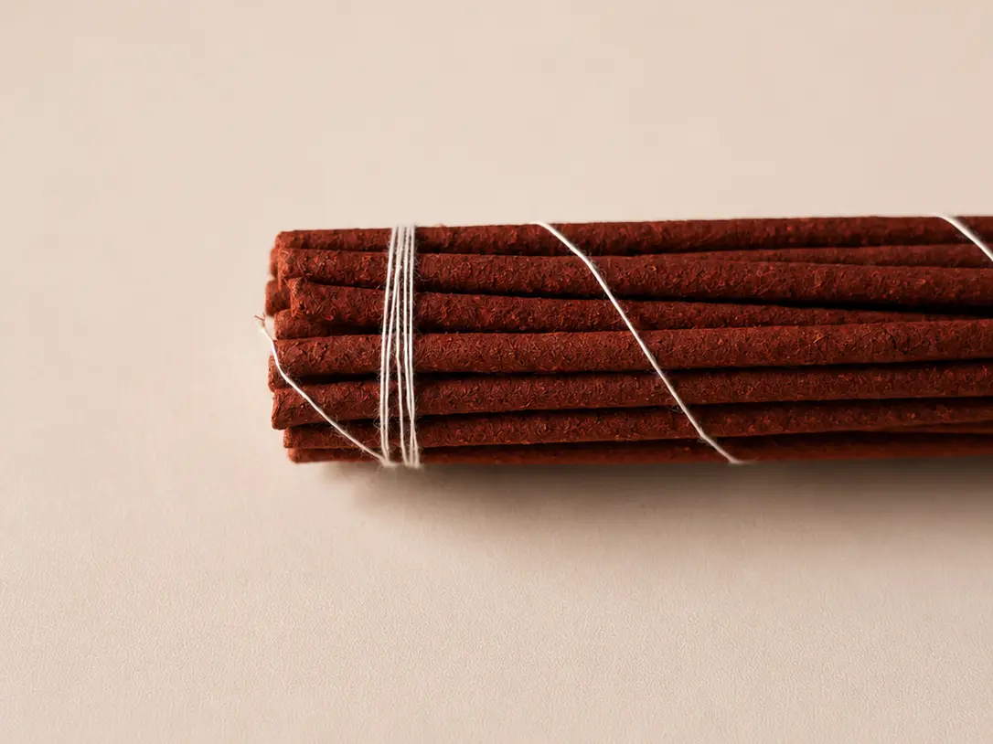 Side view of a bundle of reddish-brown incense sticks tied with white thread