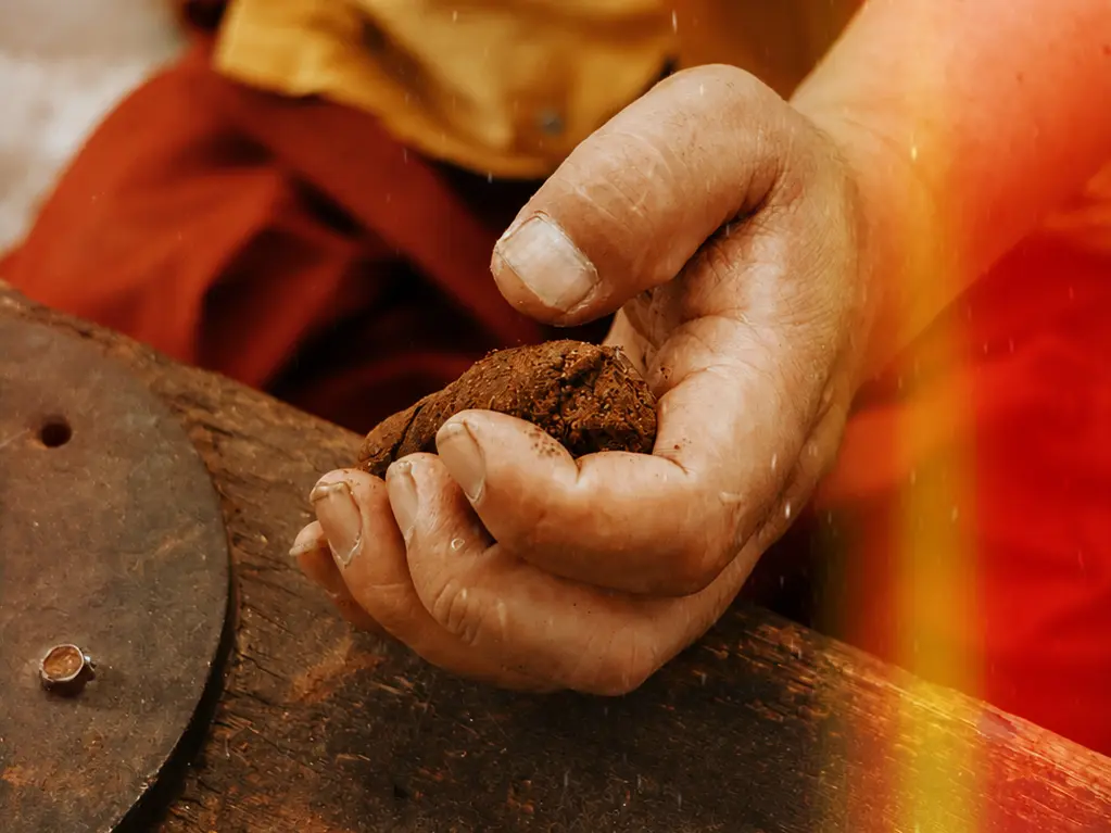 Hand holding dark material above a worn surface, with a person in yellow and red clothing