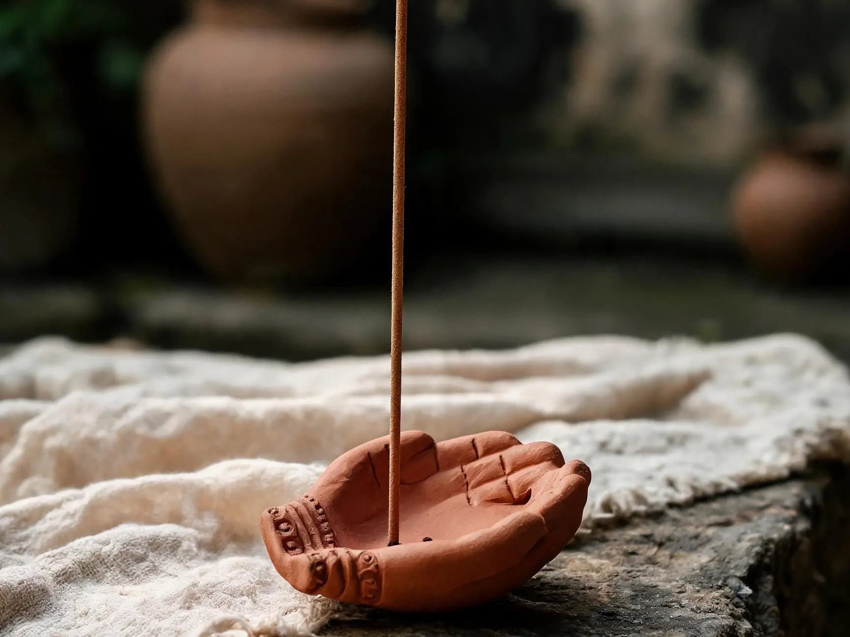 Pema hand-shaped red clay incense holder beside brown incense sticks and a paper-wrapped incense bundle