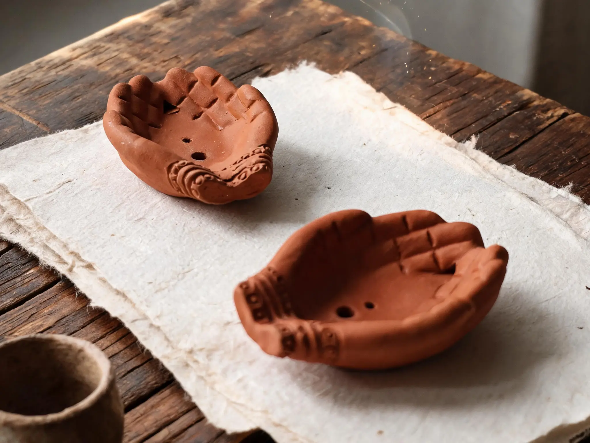 Three hand-shaped red terracotta incense holders arranged on a light surface in warm sunlight