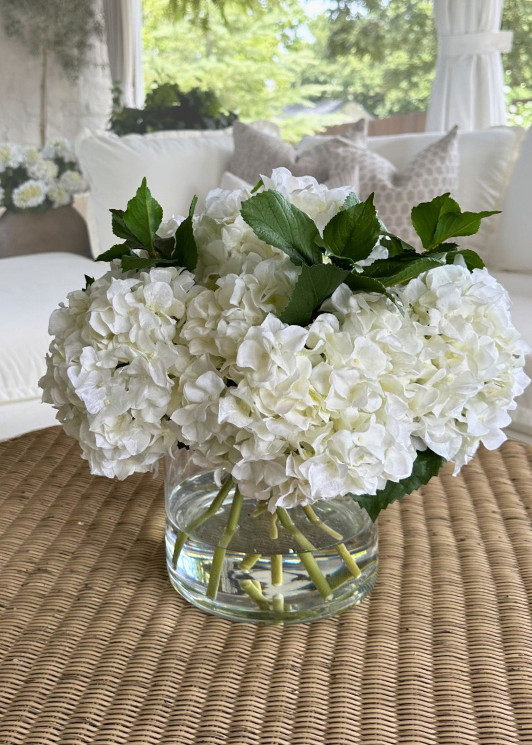 Bouquet of white hydrangea flowers in a clear vase on a woven table