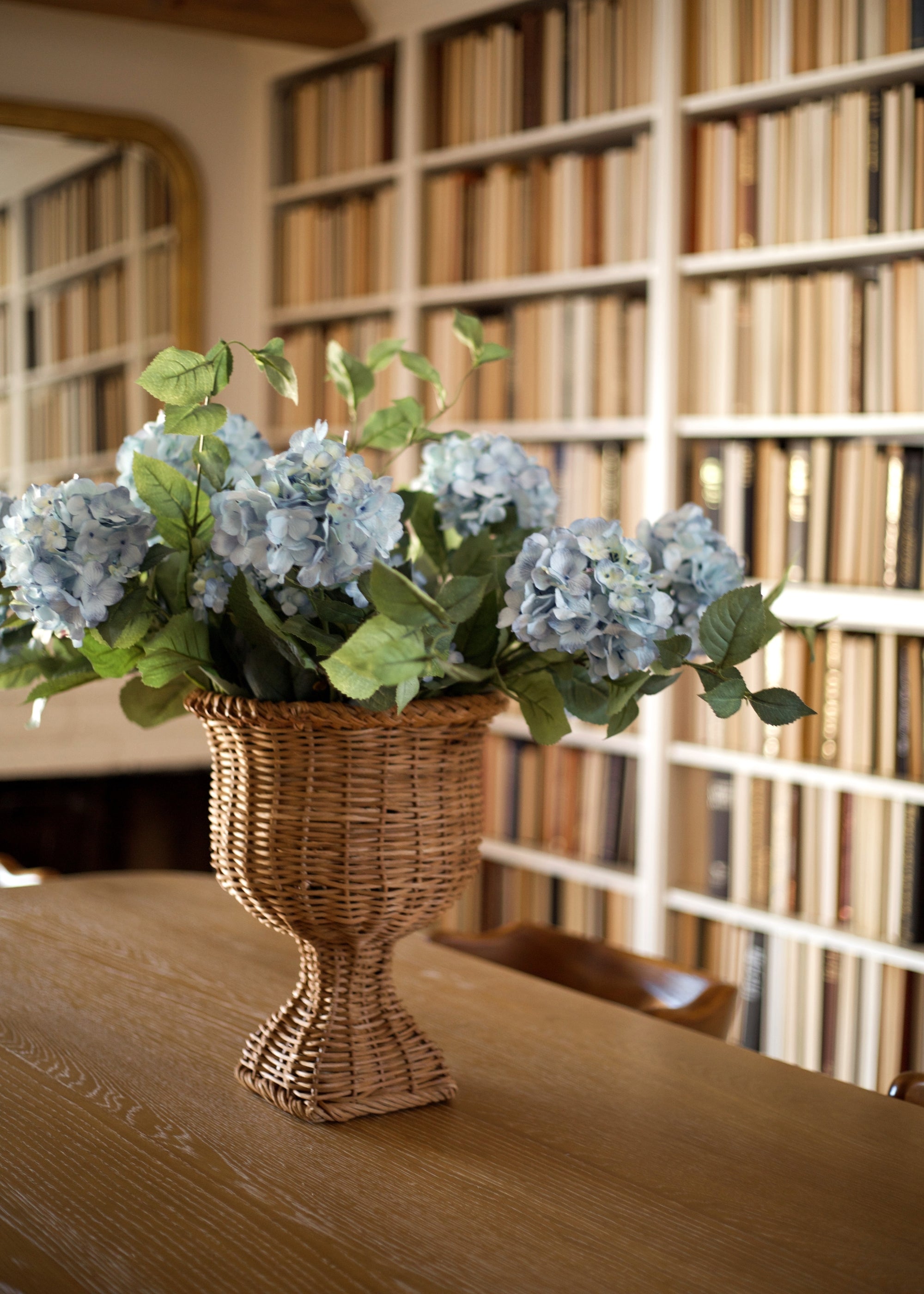 Vase with artificial blue hydrangeas on a table in front of a bookshelf