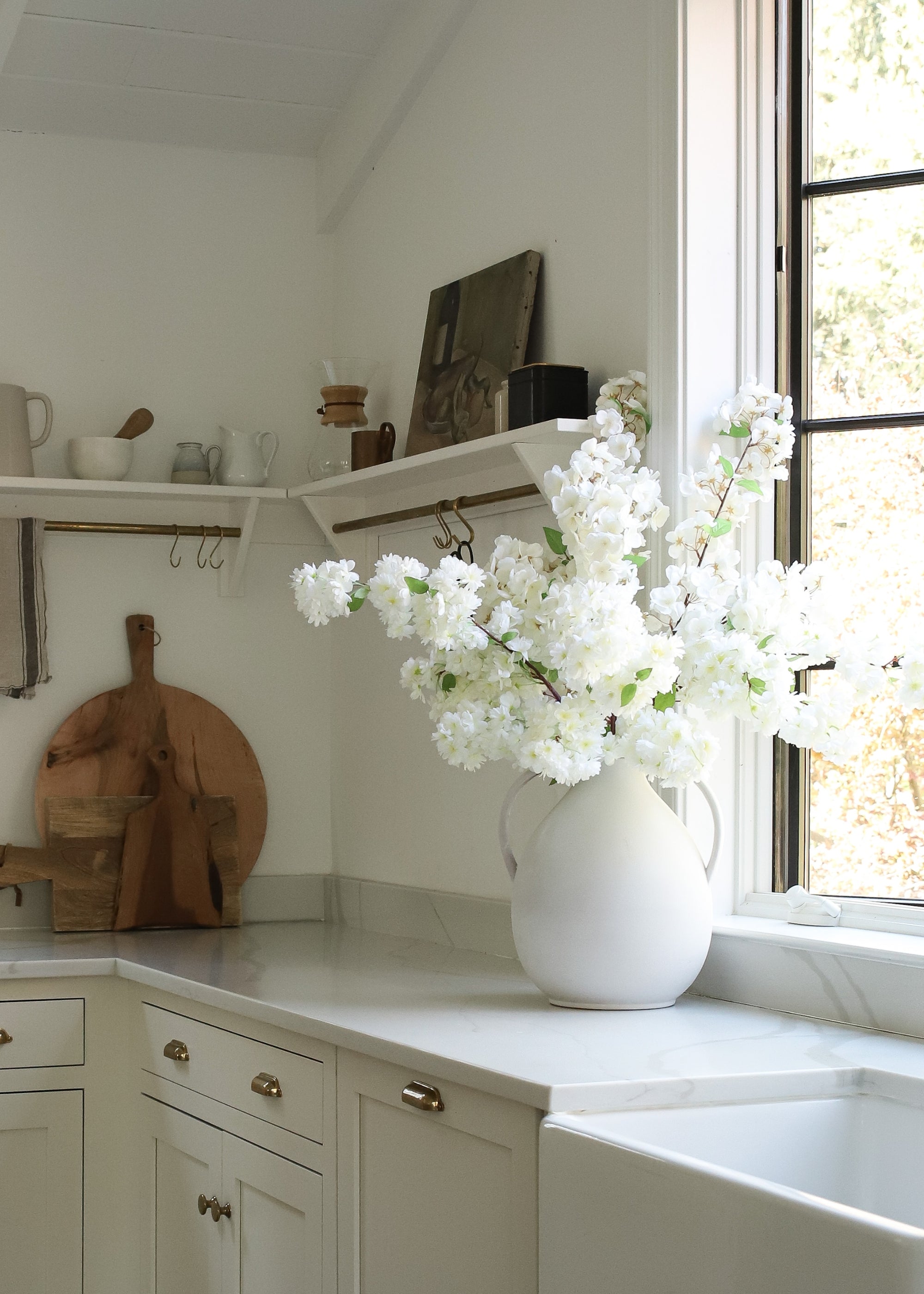 White cherry blossom flowers in a vase on a kitchen counter with a window in the background