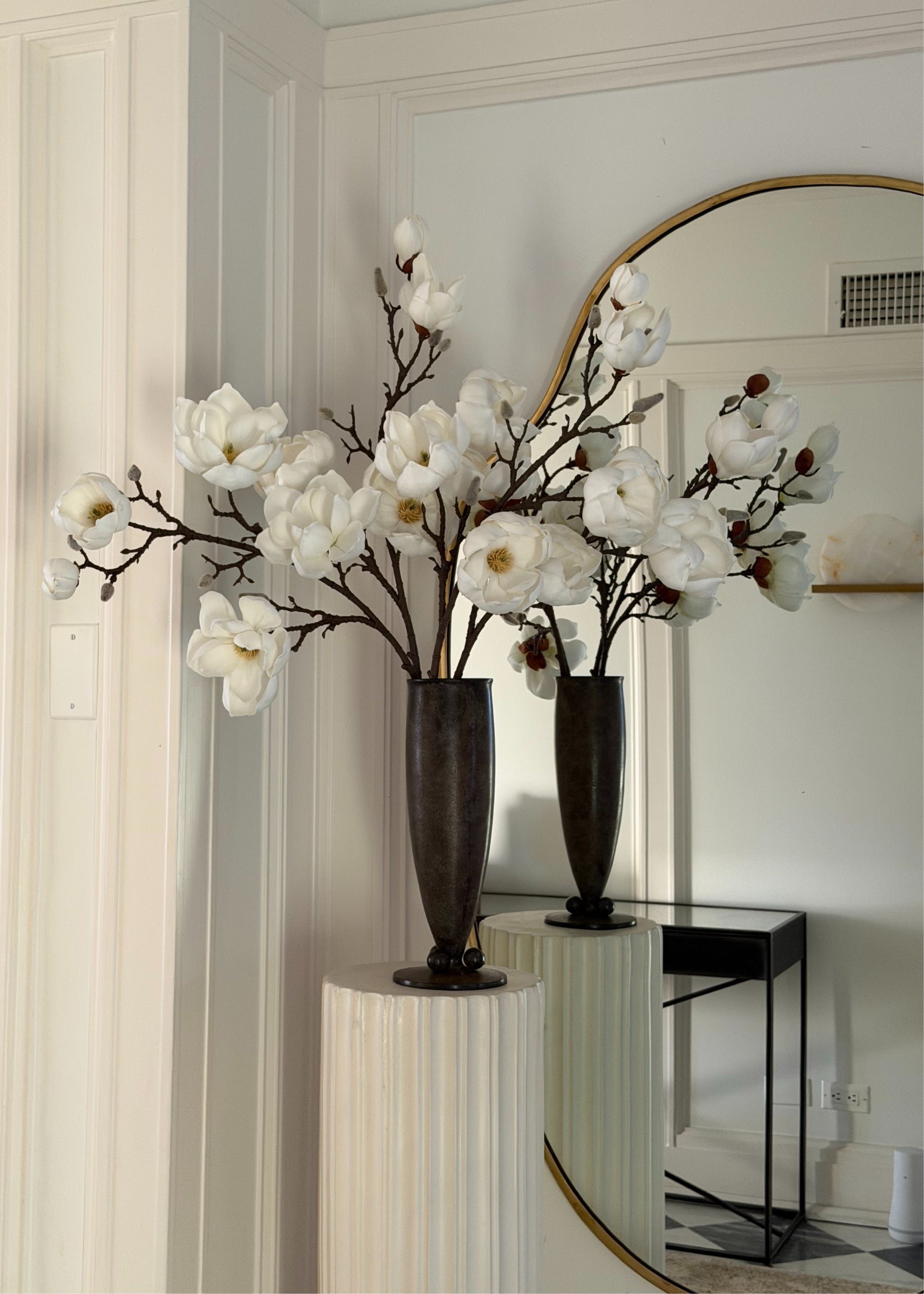white faux magnolia flowers in black vase on a pedestal