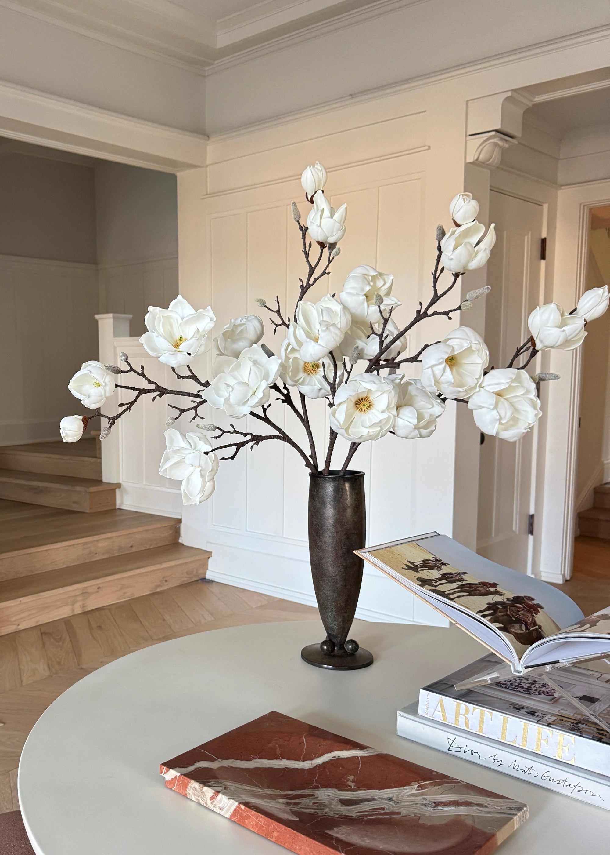 Decorative vase with white artificial magnolias on a table in a room with a staircase
