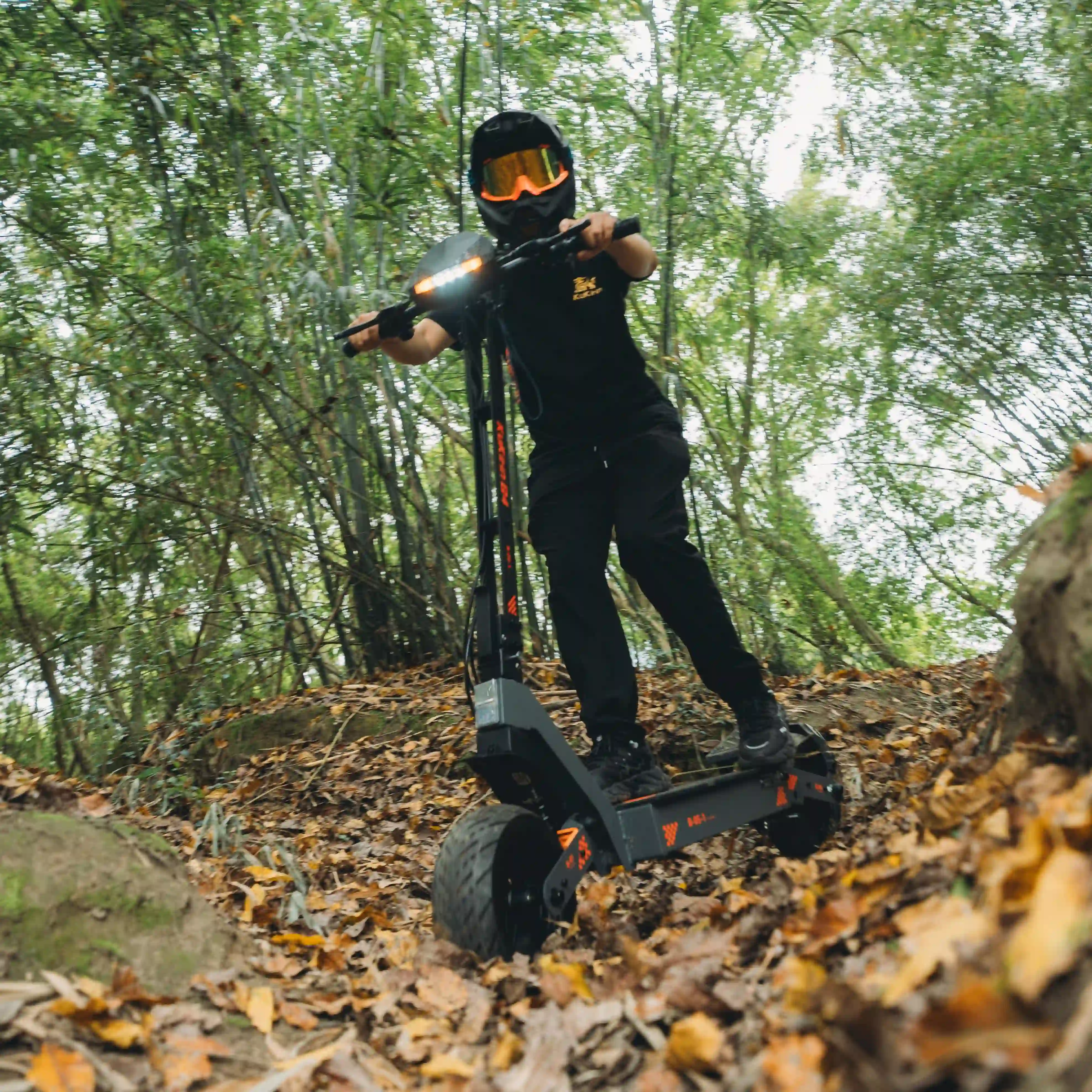 Kukirin G4 forest trail off-road riding scene, rider in full protective gear, 2000W motor, 60V 20Ah battery, 70km/h max speed, 75km max range,30° climbing ability, stable on rough leaf-covered paths, global kukirin