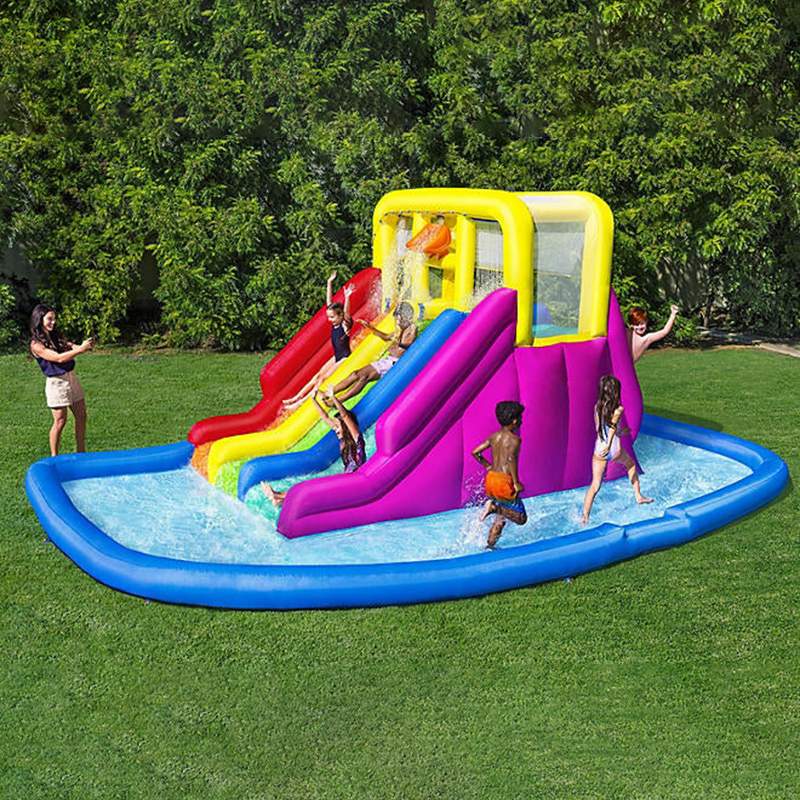 Children playing on the inflatable mega water park with triple slides and splash pool in a garden