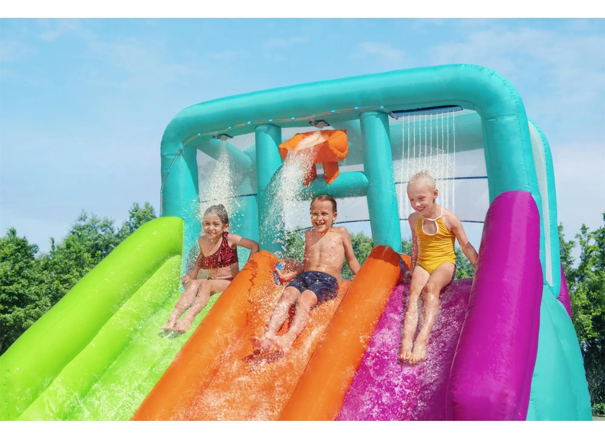 Three children racing side by side down the triple water slides with overhead dump bucket and waterfall sprinkler