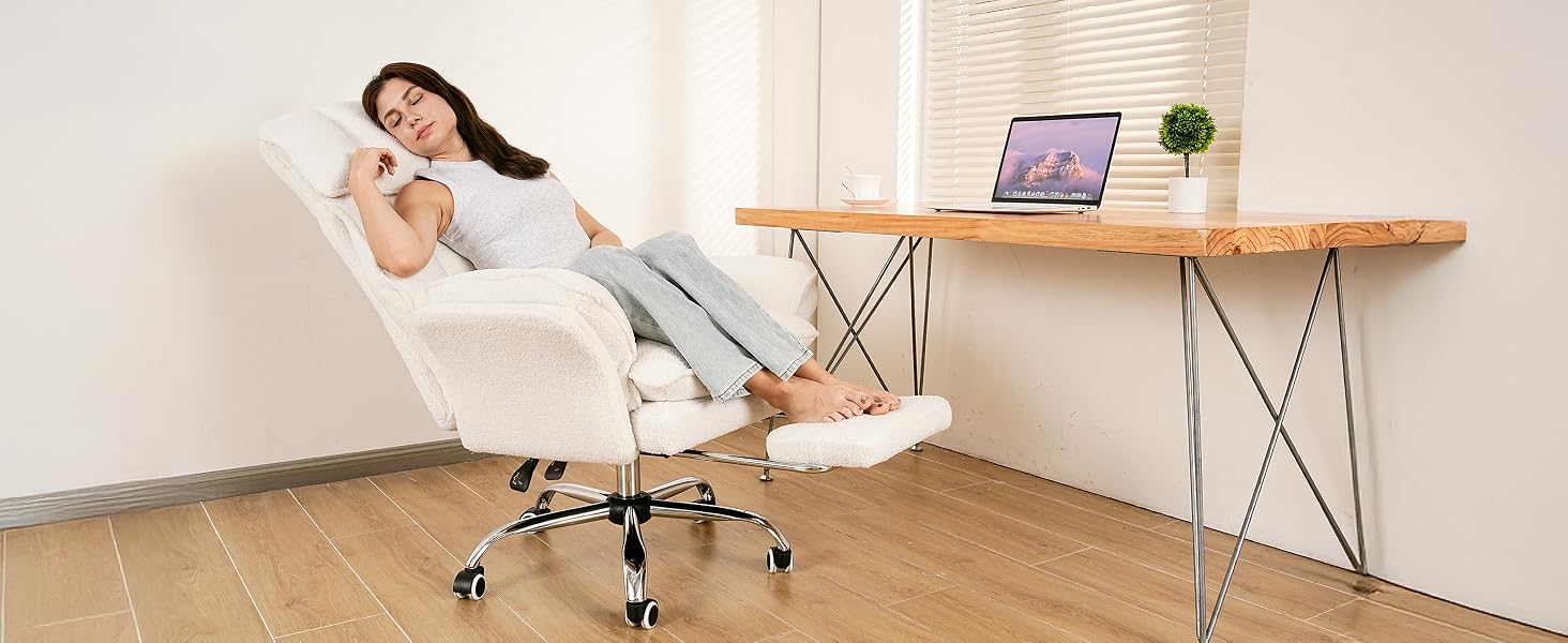 Woman resting with eyes closed on a white reclined chair with footrest extended at a wooden desk