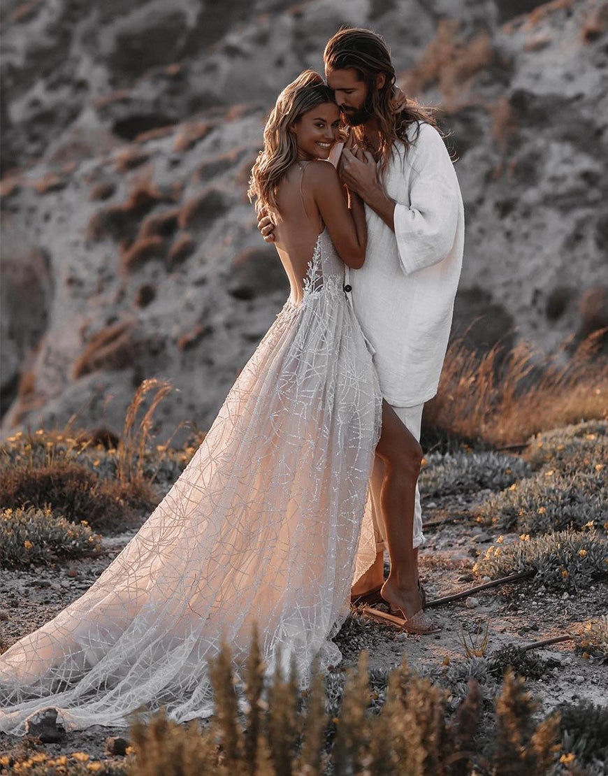 A bride in a white A-line V-neck backless Boho wedding dress with lace embellishments and a sweep train, standing close to a groom who is facing away from the camera.