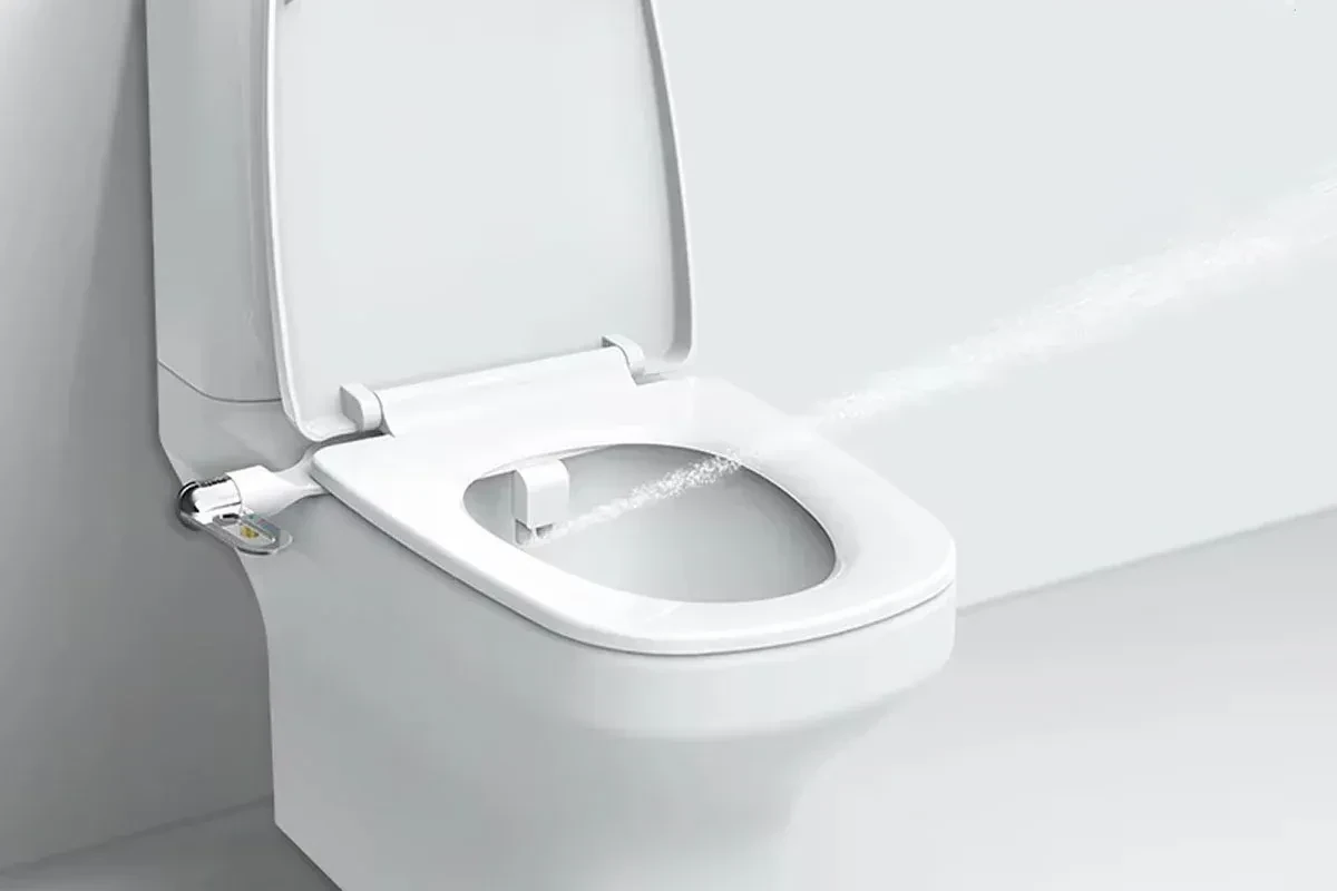 White bidet toilet seat with side control knob spraying water into open bowl.