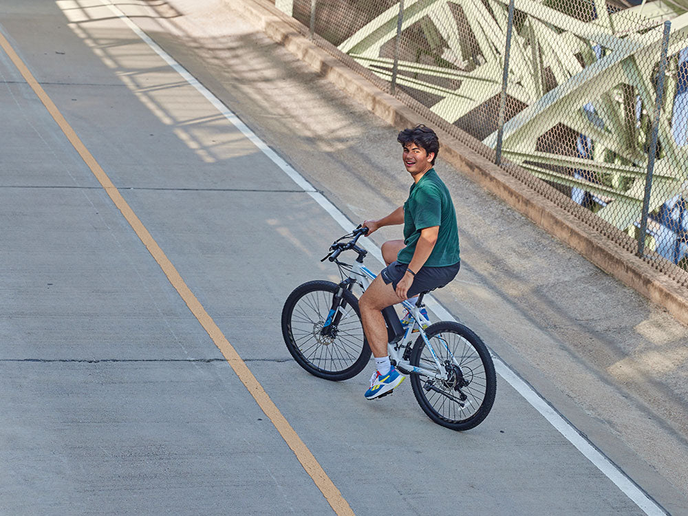A smiling person riding a QNUT e-bike through a sunny city park.