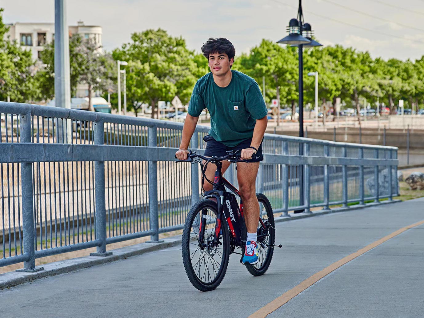 A person riding a QNUT Victor ebike through a sunny city park.