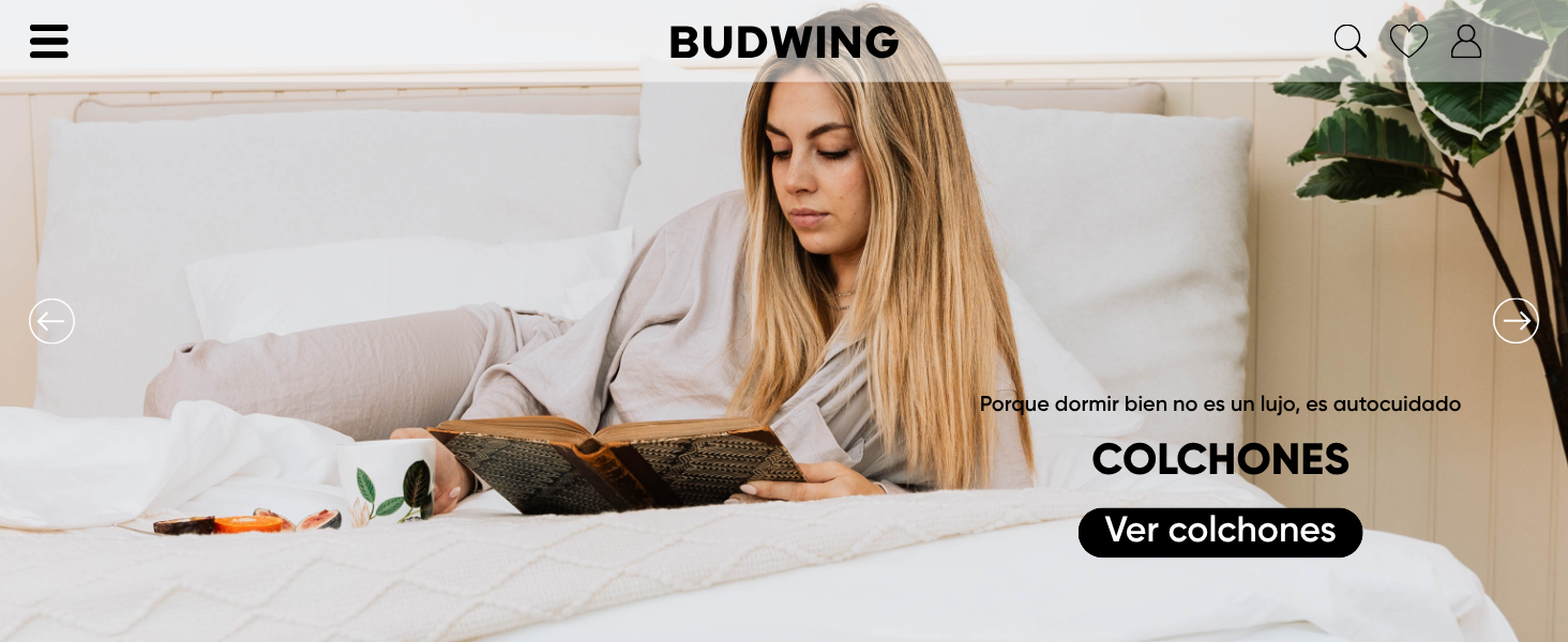 Persona recostada en ropa de cama blanca mientras lee, con los elementos de la interfaz del sitio web visibles, incluido el texto etiquetado como «COLCHONES».